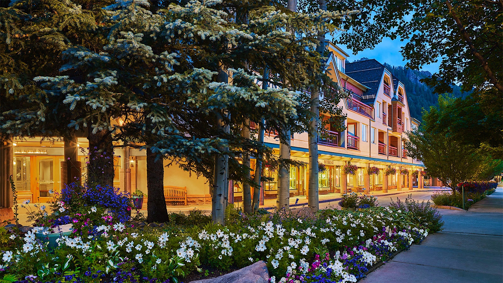 The exterior of the Little Nell hotel in Aspen, Colorado, surrounded by trees and with a view of a nearby mountain